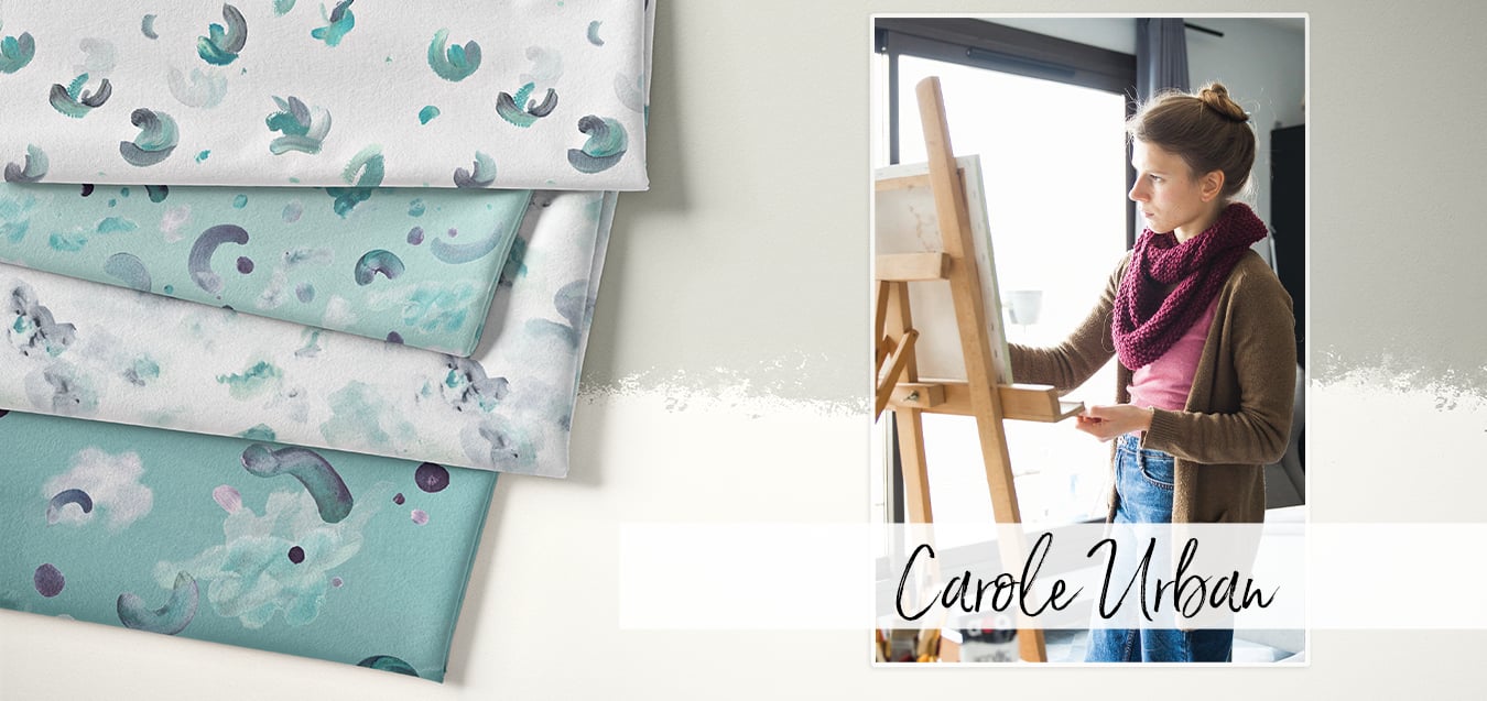 Folded fabrics with abstract watercolor brushstroke prints in teal, gray, and white, beside a photo of designer Carole Urban painting at an easel.