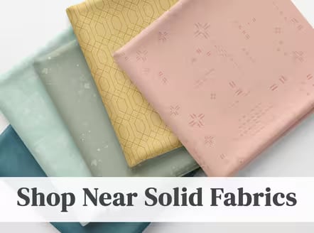 Folded fabrics in navy, sage, mustard geometric print, and blush with tonal motifs, with text "Shop Near Solid Fabrics"