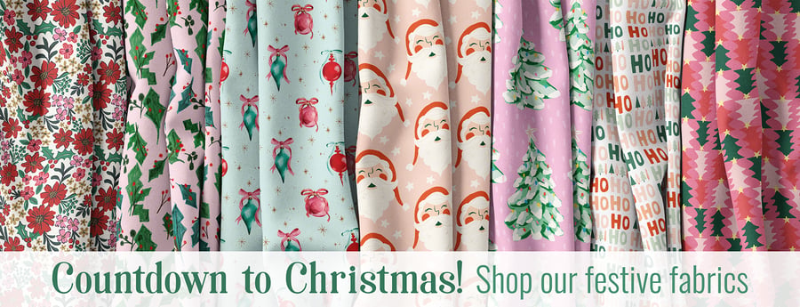 Draped fabric bolts with Christmas prints: florals, holly, ornaments, Santa faces, trees, Ho Ho Ho text, and trees pattern