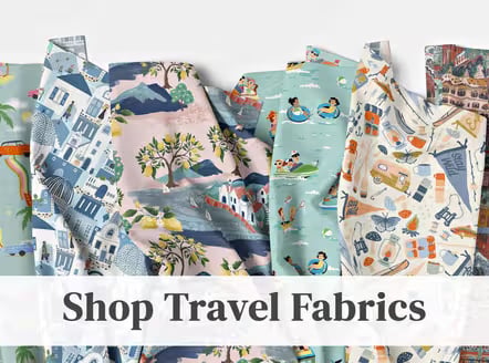 Assorted travel-themed fabrics with prints of houses, trees, beach scenes, and suitcases in blue, pink, and teal tones